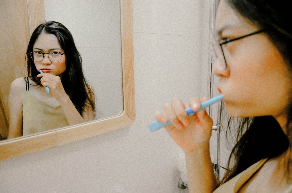 An image of a woman brushing her teeth in front of a mirror